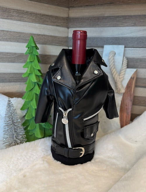 A black leather wine bottle holder with a zipper, designed to resemble a motorcycle jacket, displayed with a wine bottle inside and decorative elements in the background.